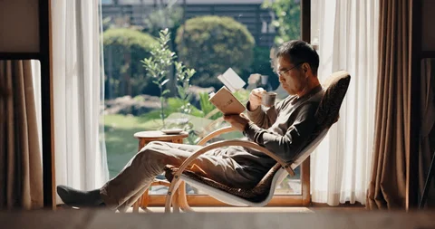 Person reading peacefully with tea by large window with natural light